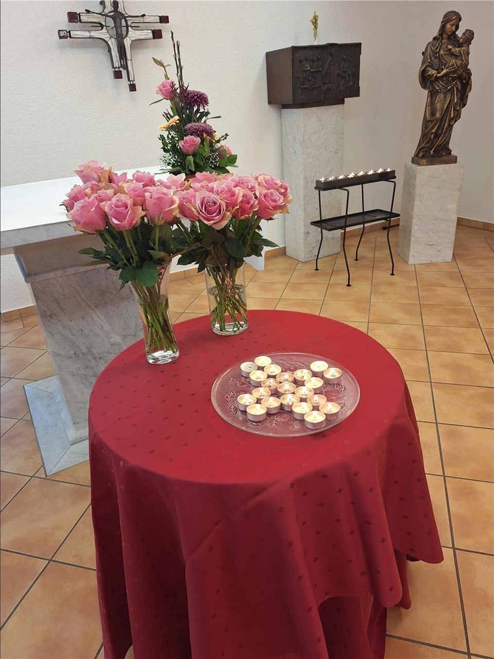 Auf einem runden Tisch mit roter Tischdecke stehen Blumen und Teelichter, die wie ein Kreuz angeordnet sind.