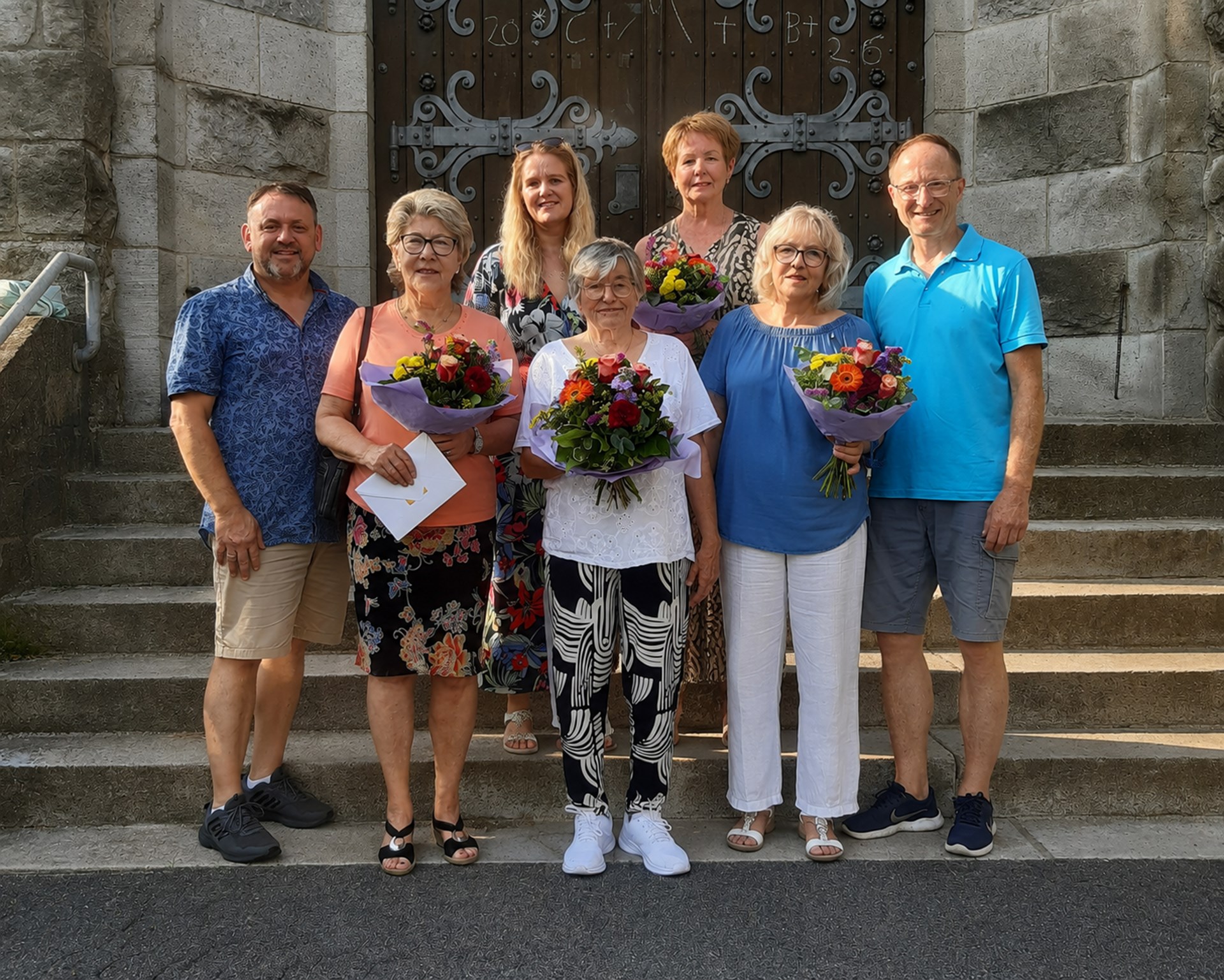 Sieben Personen - einige mit Blumensträußen - vor einem Kirchenportal nach einer Ehrung.