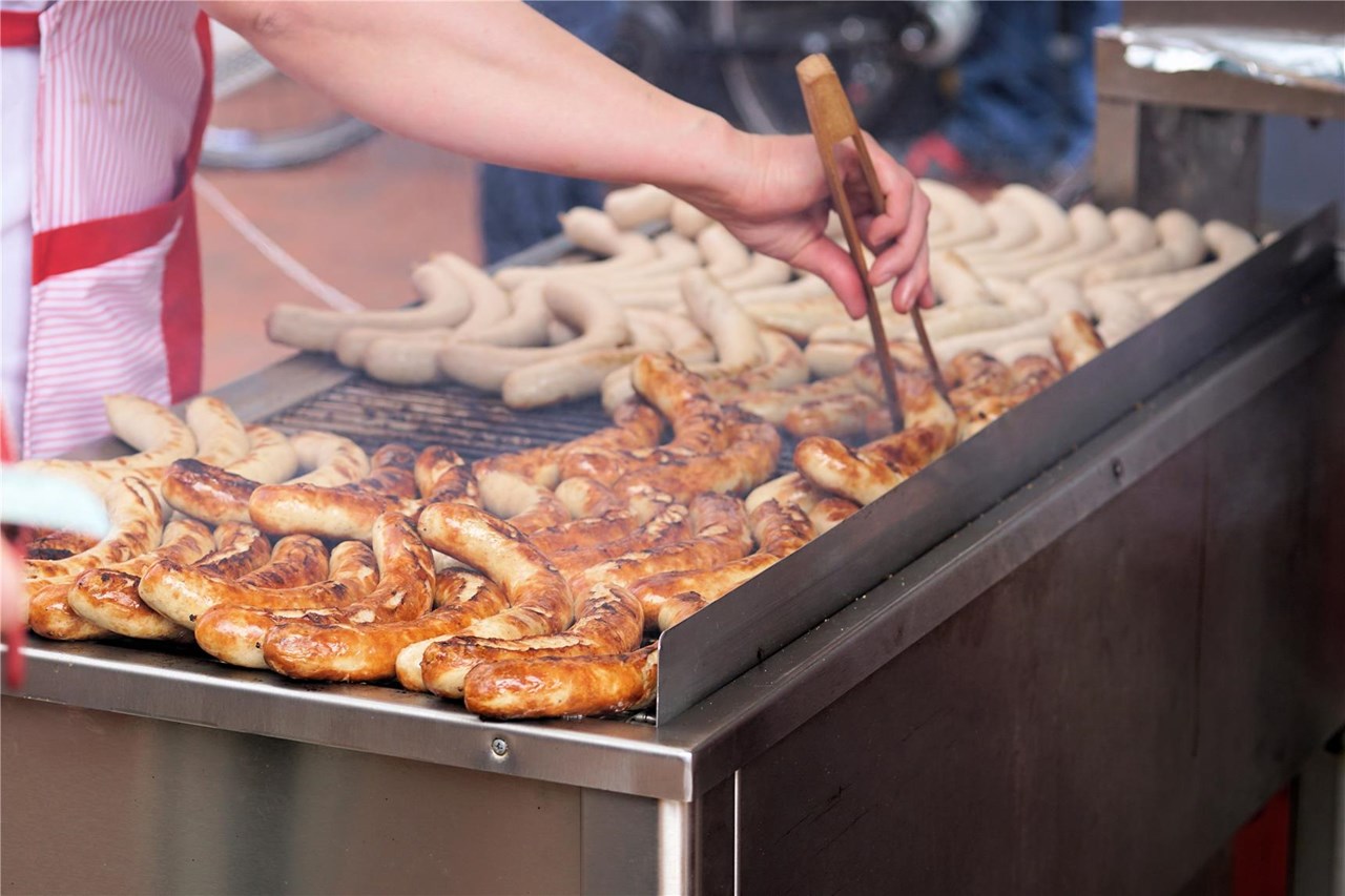 Blick auf einen Grill, auf dem viele Bratwürste liegen.