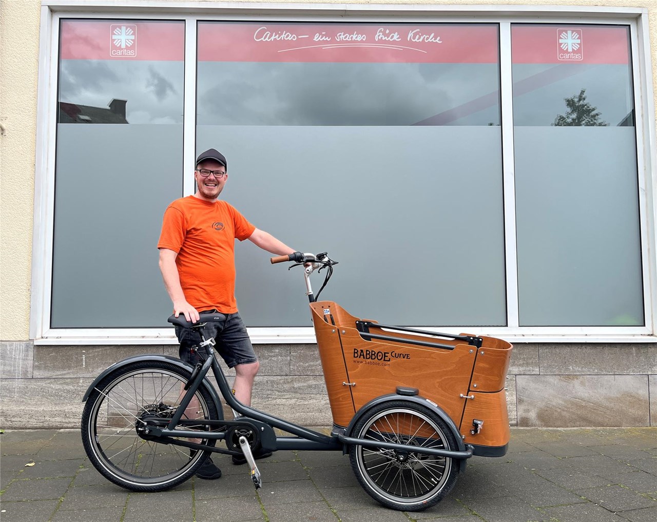David Zirwes, Mitarbeiter der Caritas-Wohnungslosenhilfe, mit dem neuen E-Lastenrad vor dem Tagesaufenthalt „Treff“ in Lahnstein.