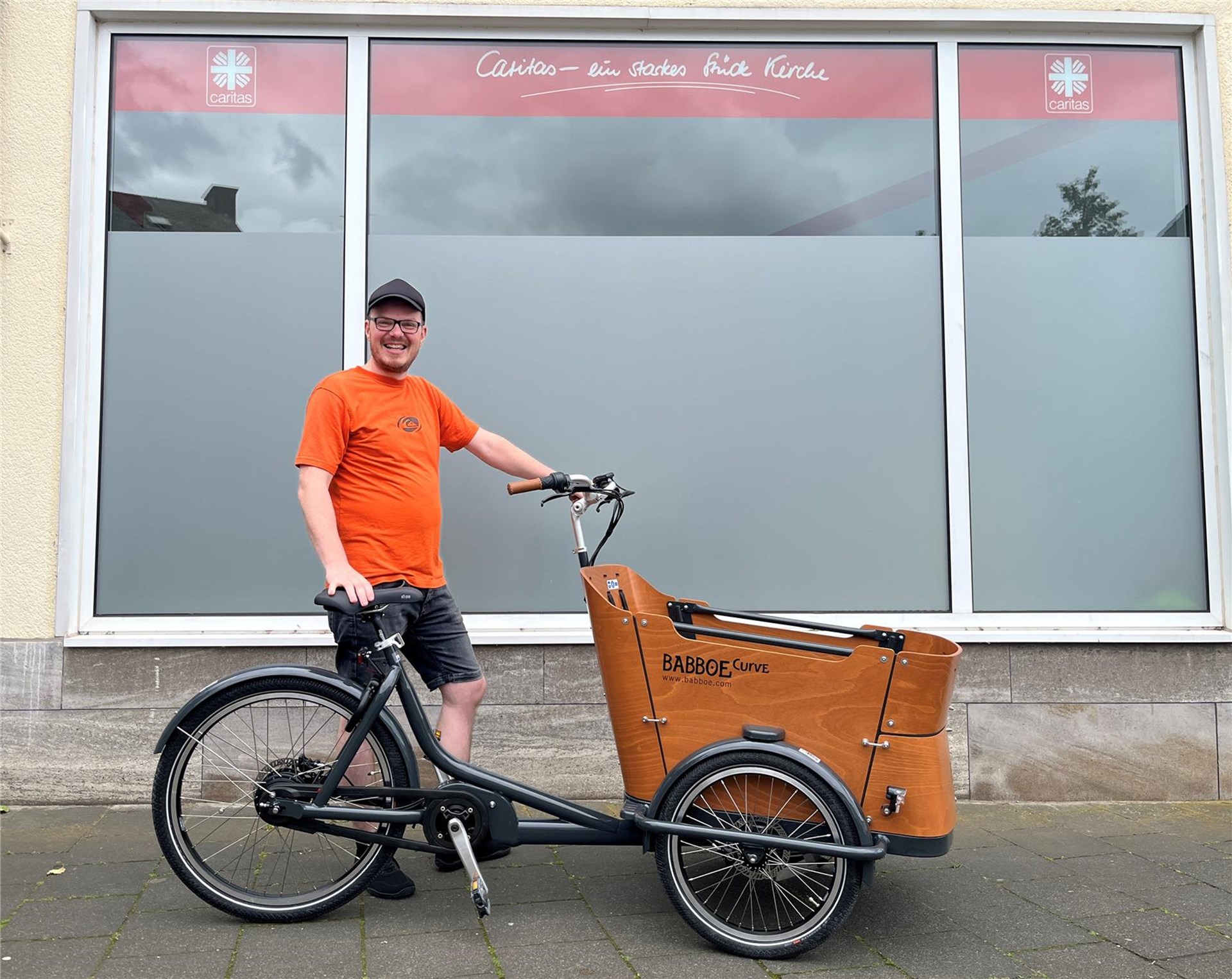 David Zirwes, Mitarbeiter der Caritas-Wohnungslosenhilfe, mit dem neuen E-Lastenrad vor dem Tagesaufenthalt „Treff“ in Lahnstein.