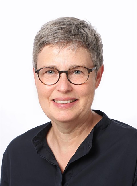 Porträtaufnahme einer Frau mit Brille, die in die Kamera lächelt.