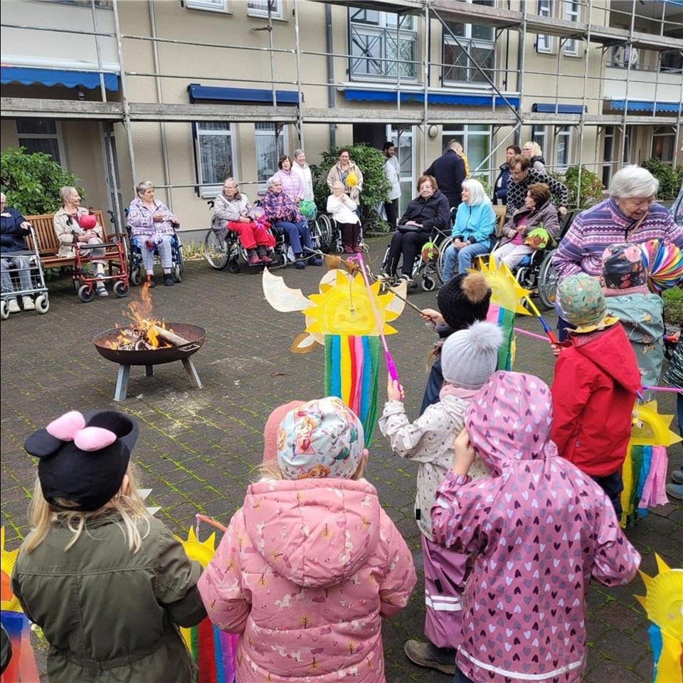 Um eine Feuerschale haben sich Kinder und Bewohner:innen mit bunten Laternen versammelt
