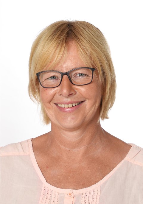 Porträtaufnahme einer Frau mit blonden Haaren und Brille, die in die Kamera lächelt.