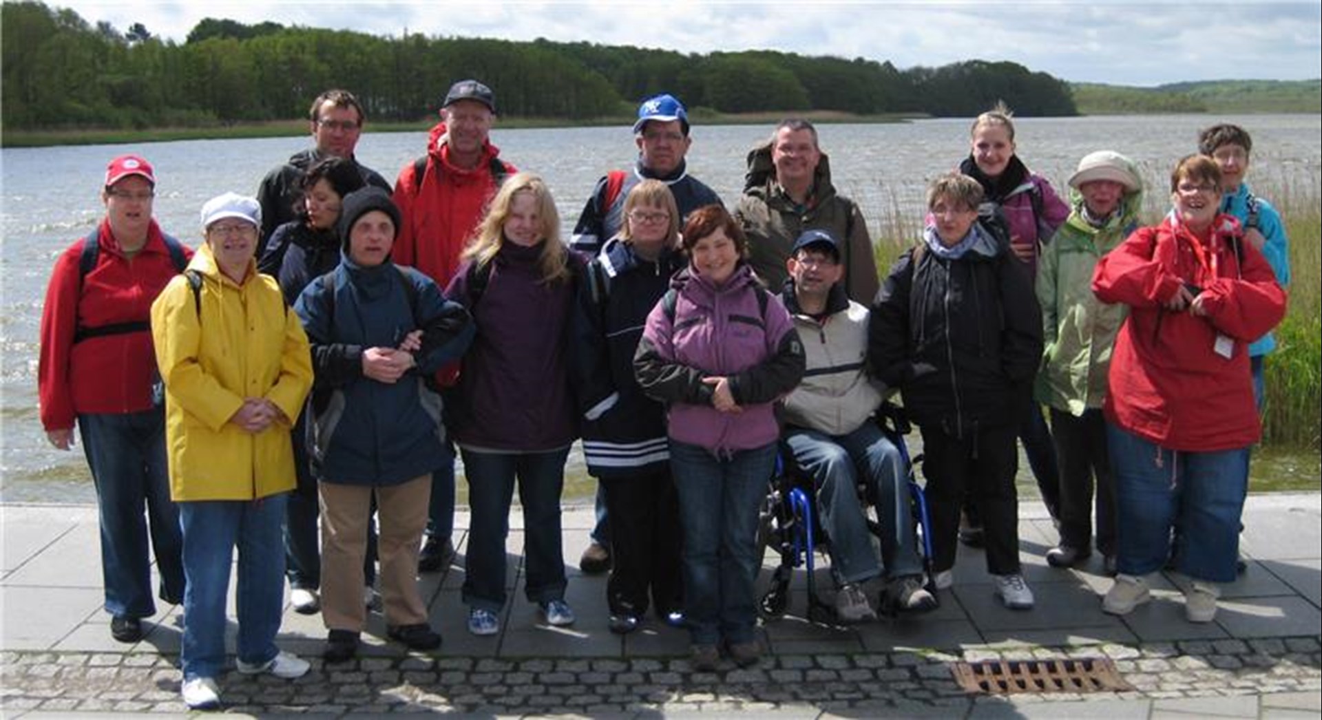 Eine Gruppe von Menschen mit Behinderungen hat sich vor einem See für ein Gruppenfoto aufgestellt.