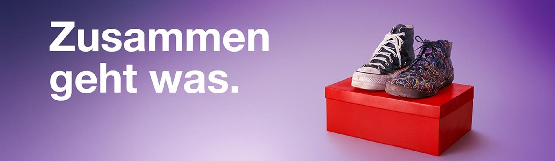 Auf einem roten Schuhkarton sind vor einem lila Hintergrund ein Paar Schuhe zu sehen. Der linke Schuh ist ein schwarzer hoher Stoffturnschuh mit weißen Schnürsenkeln, der rechte ein höherer bunt gemusterter Damenschnürschuh. Beide Schuhe sind abgenutzt. Darüber steht das Kampagnenmotto: Zusammen geht was.