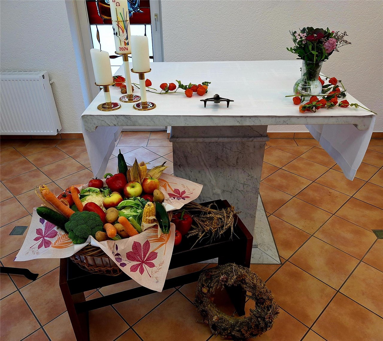 Vor dem geschmückten Altar steht auf einem Tisch ein großer Korb, prall gefüllt mit Obst und Gemüse.