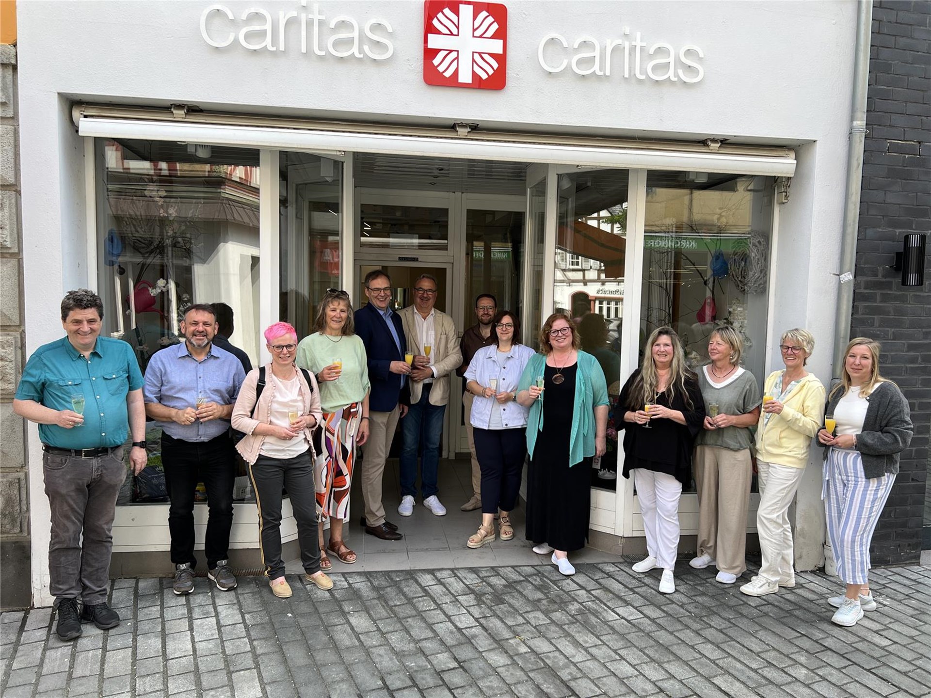 Mitarbeitende des Caritasverbandes Westerwald-Rhein-Lahn und der Pfarrei St. Peter Montabaur stehen vor dem neuen Caritas-Laden und freuen sich über die Eröffnung in der Montabaurer Innenstadt.