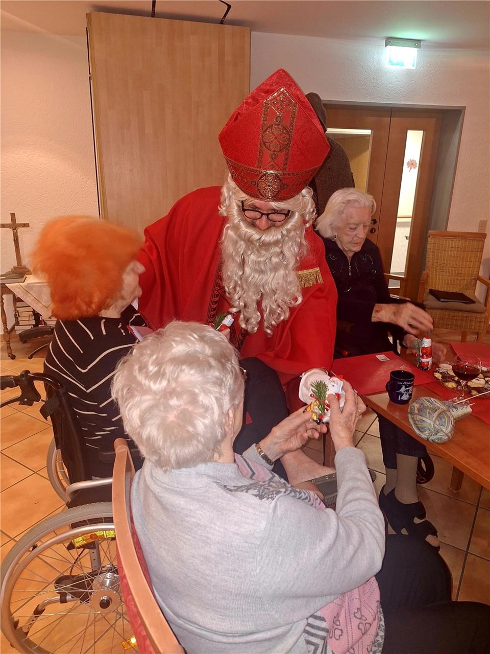 Drei Frauen sitzen an einem Tisch. Der Nikolaus verteilt Schokonikoläuse.