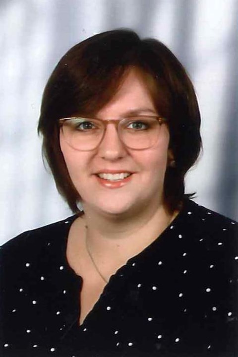 Foto einer jüngeren Frau mit braunen Haaren und Brille, die in die Kamera lächelt.